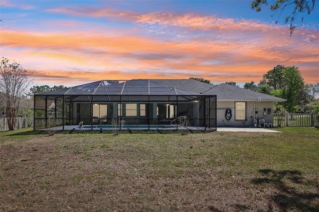 back of property at dusk with stucco siding, a fenced backyard, a yard, glass enclosure, and a patio area