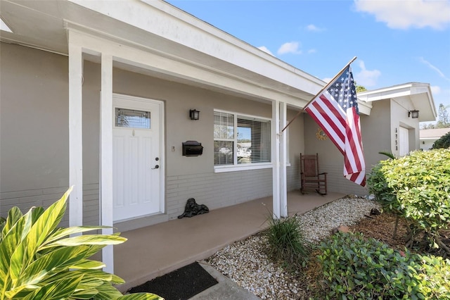 entrance to property with brick siding, covered porch, and stucco siding