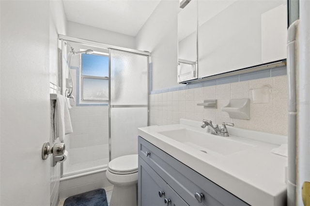 bathroom with vanity, a shower stall, wainscoting, tile walls, and toilet