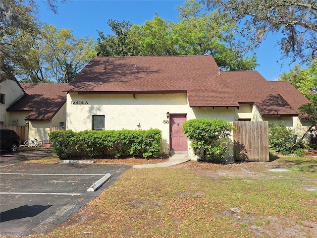 view of front of home with stucco siding, a shingled roof, a front yard, and uncovered parking