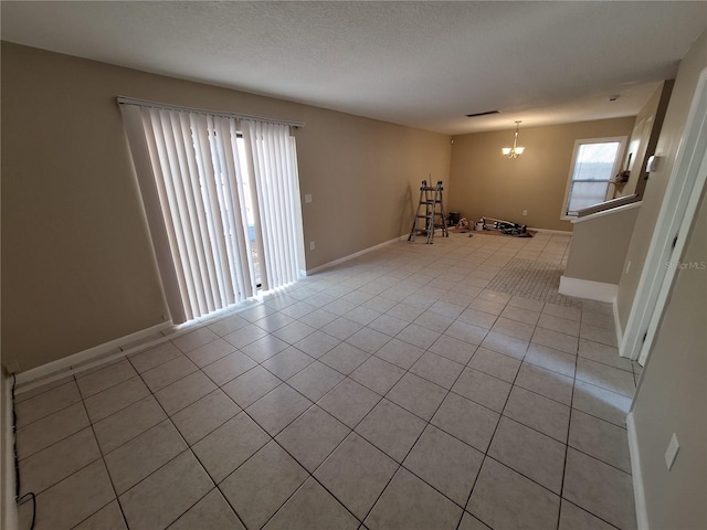 spare room with an inviting chandelier, light tile patterned flooring, baseboards, and a textured ceiling