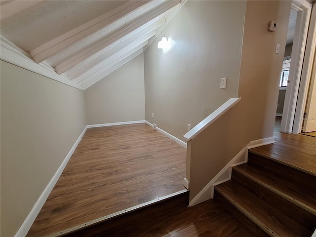 stairway featuring baseboards, wood finished floors, and vaulted ceiling