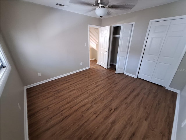 unfurnished bedroom with two closets, visible vents, baseboards, and dark wood-type flooring