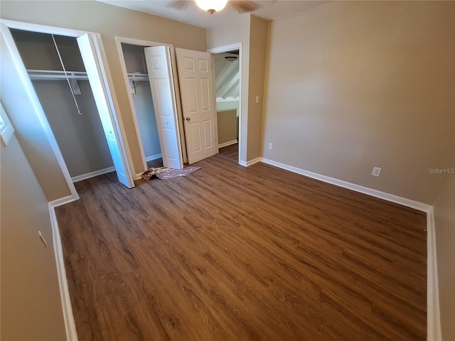 unfurnished bedroom featuring baseboards, multiple closets, and dark wood finished floors