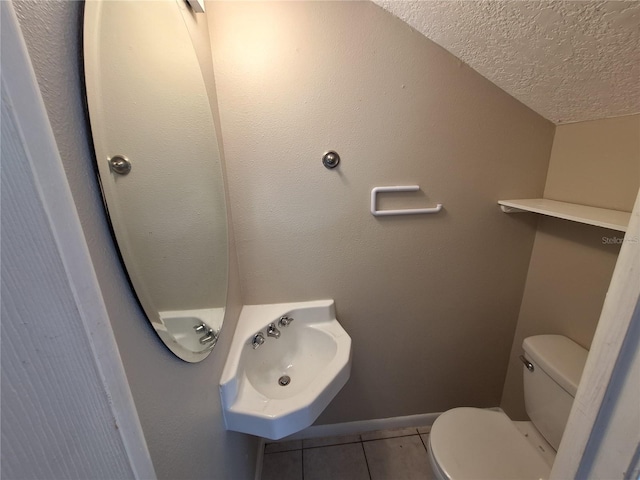 bathroom featuring baseboards, a sink, tile patterned flooring, a textured ceiling, and toilet