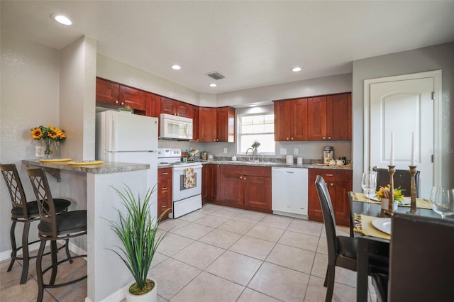 kitchen featuring white appliances, light tile patterned floors, visible vents, a breakfast bar, and reddish brown cabinets