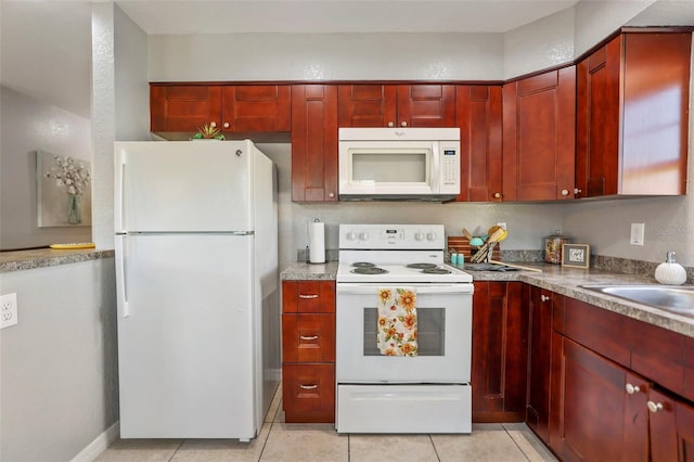 kitchen with light tile patterned floors, white appliances, and reddish brown cabinets