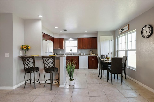 kitchen with white appliances, baseboards, a kitchen bar, and a peninsula