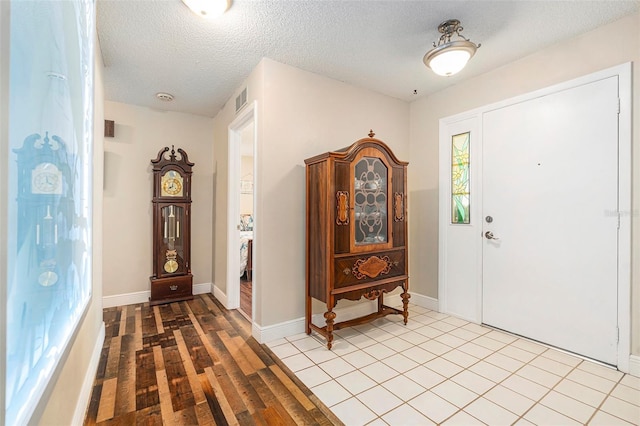 foyer with visible vents, baseboards, a textured ceiling, and wood finished floors