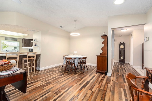 dining space with vaulted ceiling, wood finished floors, baseboards, and a textured ceiling