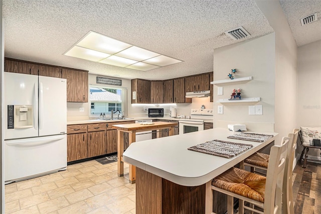 kitchen with visible vents, a sink, under cabinet range hood, white appliances, and open shelves