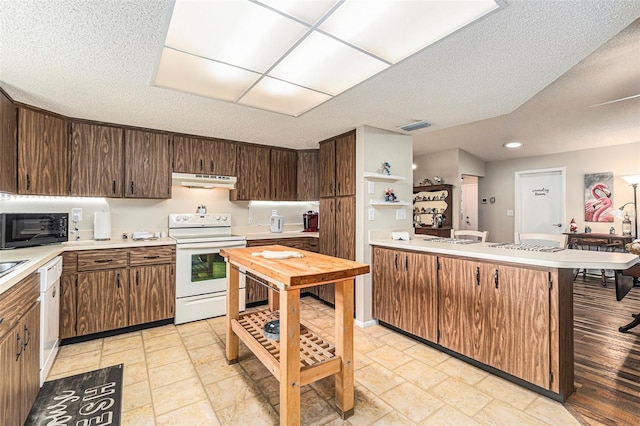 kitchen featuring under cabinet range hood, light countertops, a peninsula, white appliances, and a textured ceiling