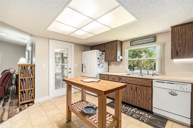 kitchen featuring a sink, white appliances, a textured ceiling, and light countertops