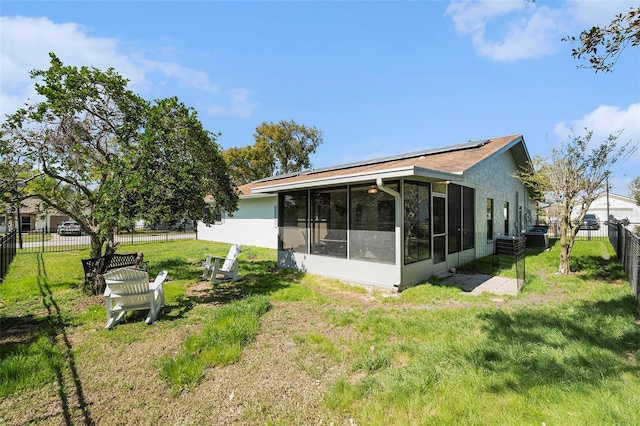 back of house with solar panels, a lawn, a fenced backyard, and a sunroom