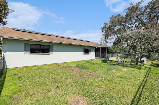 rear view of house featuring solar panels, a yard, a sunroom, and stucco siding