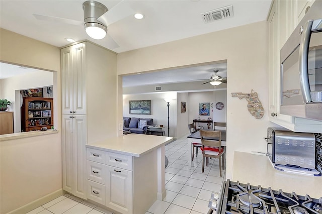 kitchen with visible vents, a ceiling fan, stainless steel microwave, a peninsula, and light countertops