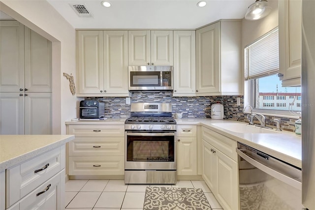 kitchen with light countertops, light tile patterned floors, decorative backsplash, stainless steel appliances, and a sink