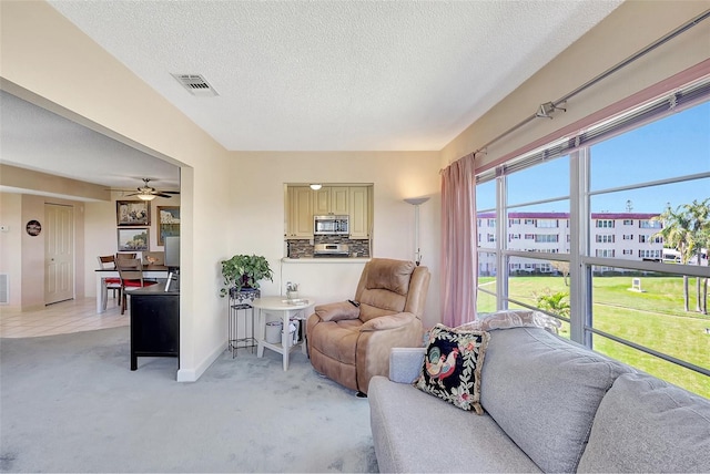 living area with visible vents, baseboards, light colored carpet, a textured ceiling, and a ceiling fan