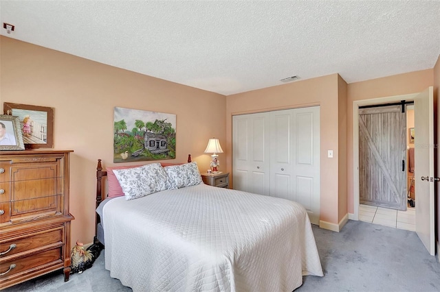 carpeted bedroom with baseboards, visible vents, a closet, a textured ceiling, and a barn door