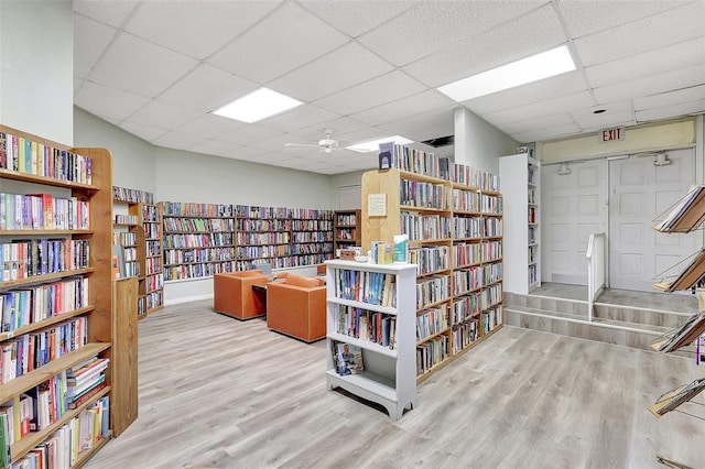 miscellaneous room featuring ceiling fan, a drop ceiling, wood finished floors, and wall of books