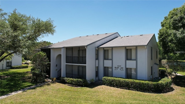 back of house featuring stucco siding, a shingled roof, and a yard