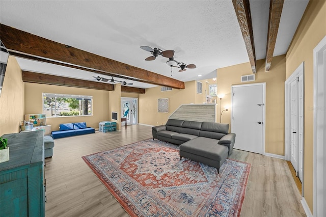 living room featuring beamed ceiling, light wood-style flooring, visible vents, and ceiling fan