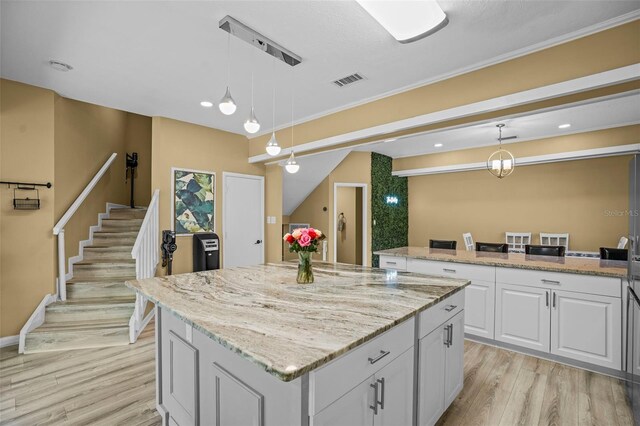 kitchen featuring visible vents, light wood-style flooring, light stone counters, a kitchen island, and white cabinetry