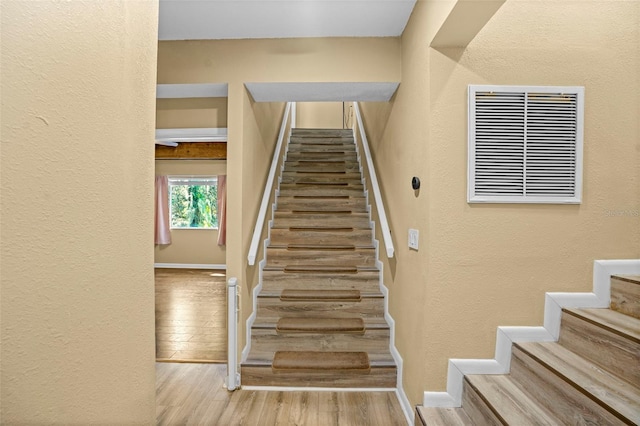 stairway with visible vents, baseboards, wood finished floors, and a textured wall