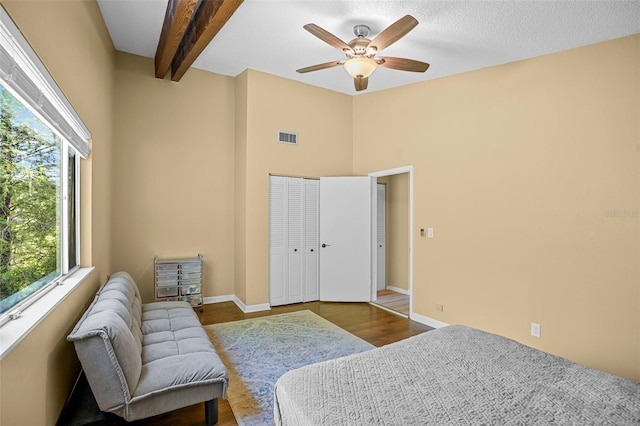 bedroom featuring wood finished floors, visible vents, baseboards, vaulted ceiling with beams, and ceiling fan