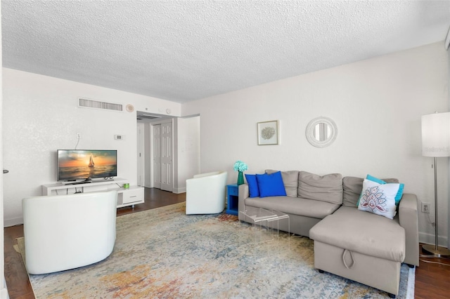 living room with visible vents, baseboards, a textured ceiling, and wood finished floors