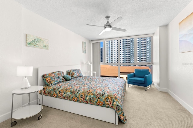 carpeted bedroom featuring ceiling fan, a wall of windows, baseboards, and a textured ceiling