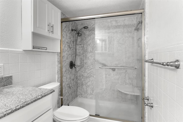 full bathroom featuring vanity, a stall shower, a textured ceiling, tile walls, and toilet