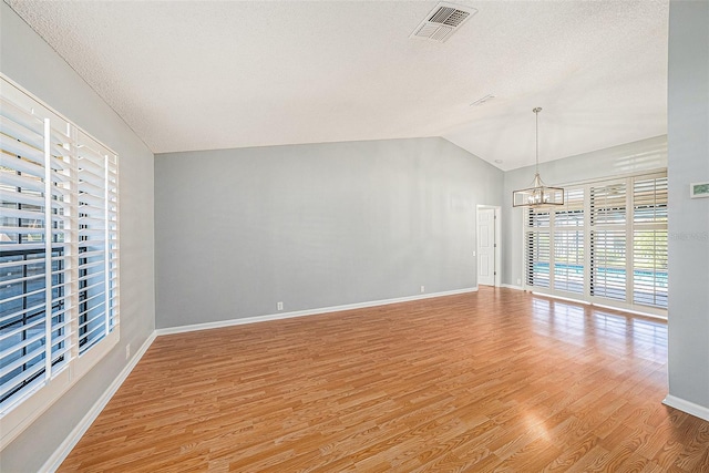 unfurnished room with baseboards, visible vents, light wood-style flooring, vaulted ceiling, and a chandelier