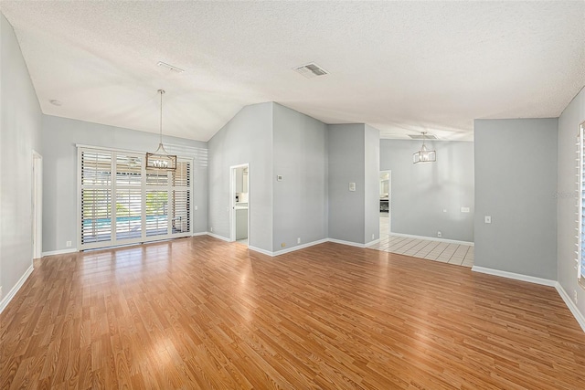 unfurnished living room with visible vents, light wood-type flooring, vaulted ceiling, an inviting chandelier, and a textured ceiling