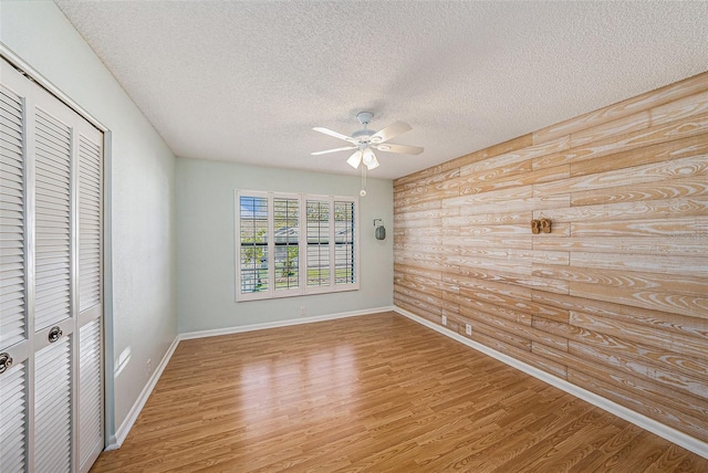 unfurnished bedroom with light wood-style flooring, a ceiling fan, a textured ceiling, a closet, and baseboards