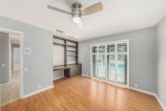 unfurnished bedroom featuring light wood finished floors, visible vents, baseboards, built in desk, and a textured ceiling