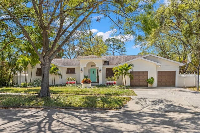 view of front facade featuring stucco siding, driveway, fence, an attached garage, and a shingled roof