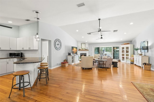 living area with lofted ceiling, light wood-style floors, visible vents, and a warm lit fireplace