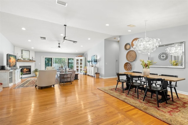 dining area with vaulted ceiling, a fireplace, visible vents, and light wood-type flooring