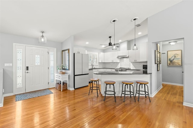 kitchen featuring visible vents, under cabinet range hood, a peninsula, freestanding refrigerator, and white cabinets