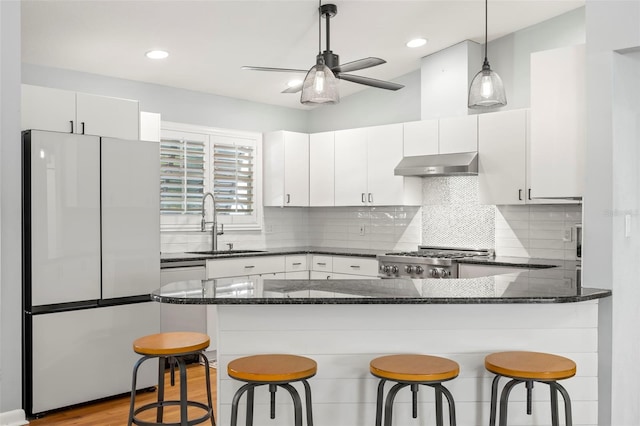 kitchen featuring freestanding refrigerator, a sink, hanging light fixtures, under cabinet range hood, and range