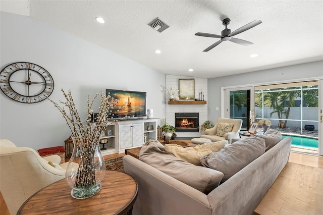 living area with a brick fireplace, wood finished floors, visible vents, and a textured ceiling