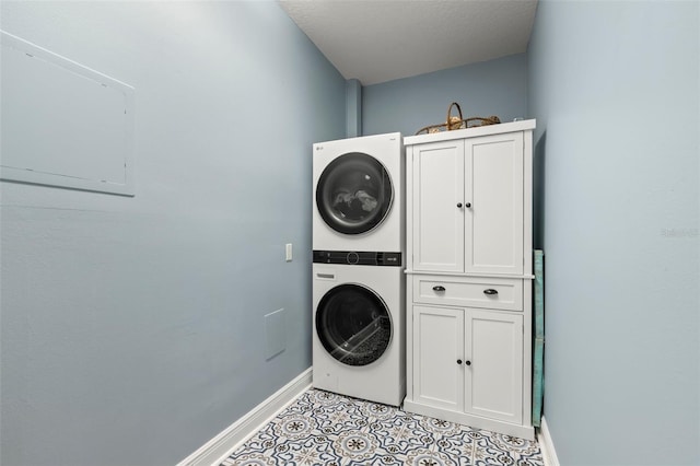 clothes washing area featuring stacked washer and dryer, light tile patterned floors, cabinet space, and baseboards