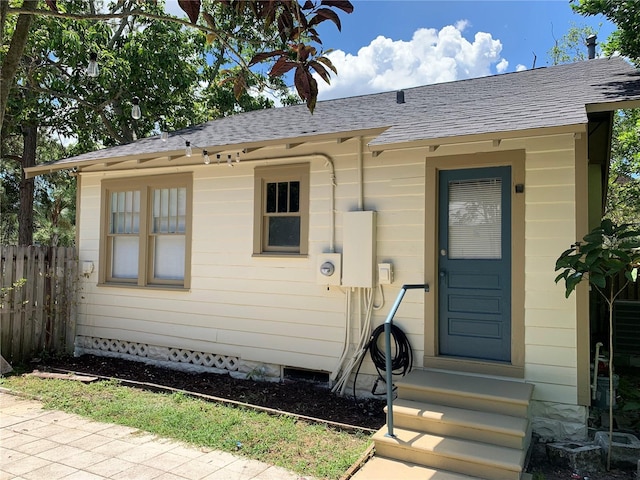 view of exterior entry with roof with shingles and fence