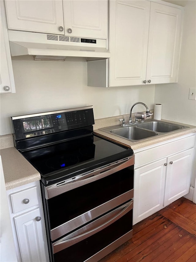 kitchen with dark wood-type flooring, under cabinet range hood, range with two ovens, white cabinets, and a sink