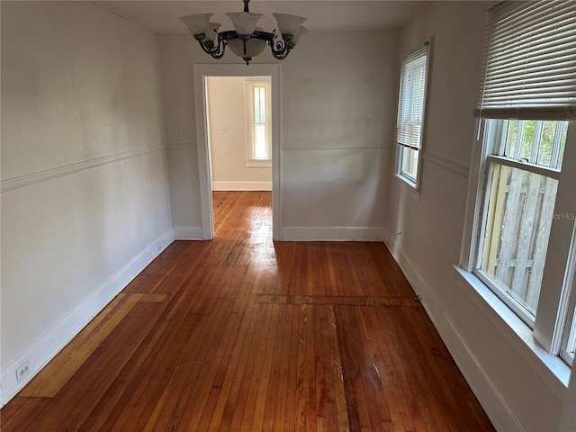 unfurnished dining area featuring an inviting chandelier, baseboards, and wood-type flooring