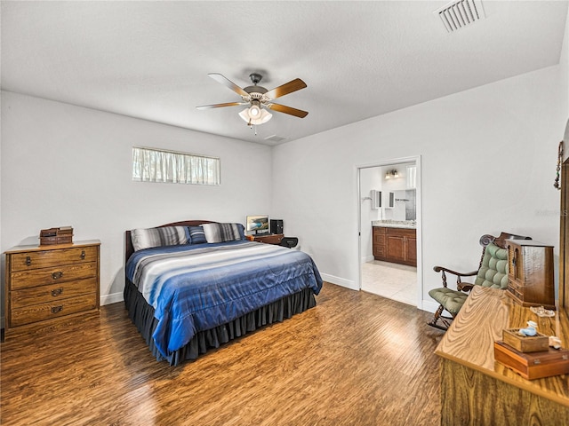 bedroom featuring ensuite bath, wood finished floors, visible vents, and baseboards