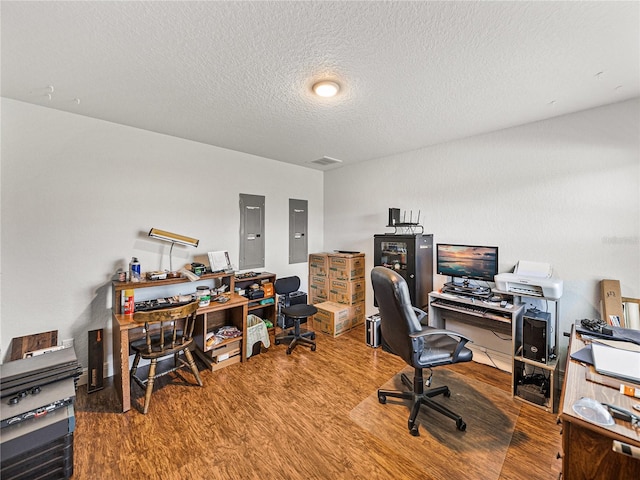 home office with electric panel, wood finished floors, visible vents, and a textured ceiling