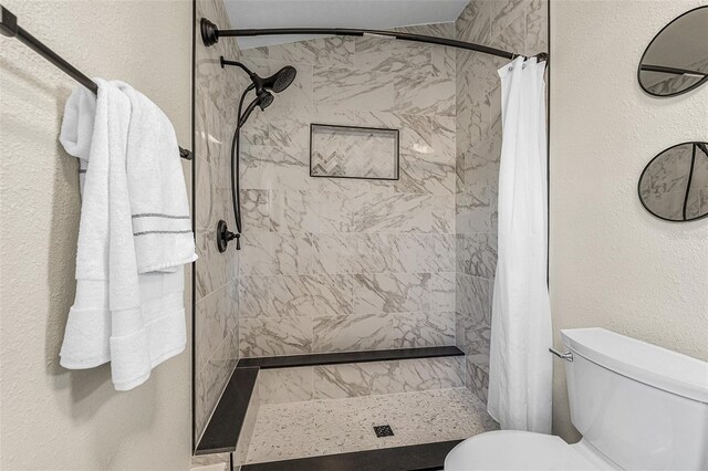 full bath with toilet, a shower stall, and a textured wall