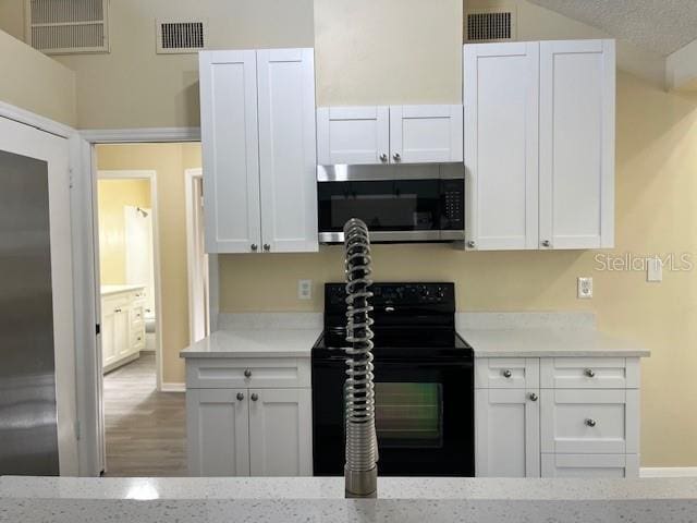 kitchen featuring stainless steel microwave, black electric range oven, white cabinetry, and visible vents